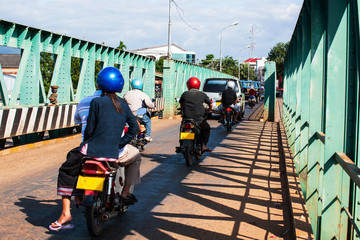 Naklejka na ściany i meble Laotians people riding motorcycles and driving cars across over the old bridge.