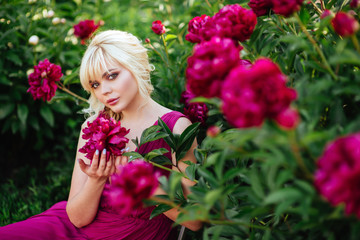 Outdoor close up portrait of beautiful young woman with long blonde hair, makeup, posing in the blooming garden. Female spring fashion concept
