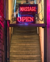 A 'Massage Open' sign hanging in the window of a massage parlour with blue and red LED lights.