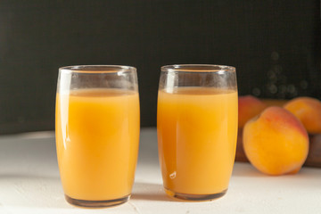 two peach juice glasses and  peaches  on white table and black backdrop