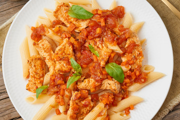 Penne pasta, chicken or turkey fillet, tomato sauce with basil leaves on old rustic wooden background. Top view, close up