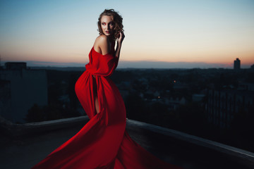 Fashion vogue style portrait of young stunning woman posing in red dress in sunset lightning....
