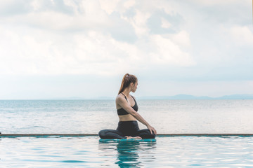 Fototapeta na wymiar Happy Asian woman wearing black sport wear practice yoga Seated Twist pose on the pool above the beach with beautiful sea in Tropical island,Feeling comfortable and relax in holiday,Vacations Concept