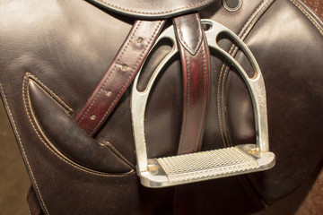 Metal stirrups and leather push-ups on a competitive saddle of dark brown color