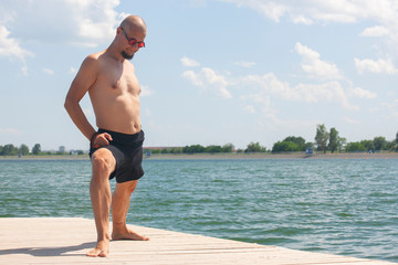 Young man doing yoga and meditating in warrior pose on beach