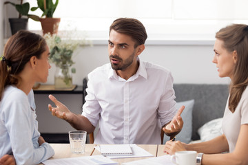 Angry businessman arguing with female subordinate at group business meeting