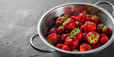 Fresh juicy red strawberries in stainless steel colander on Dark grey black slate background 