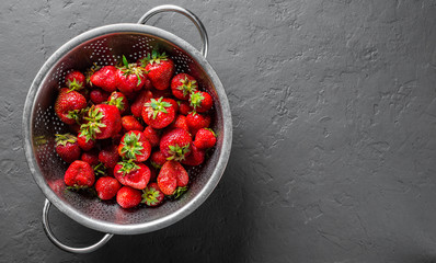 Fresh juicy red strawberries in stainless steel colander on Dark grey black slate background  - obrazy, fototapety, plakaty