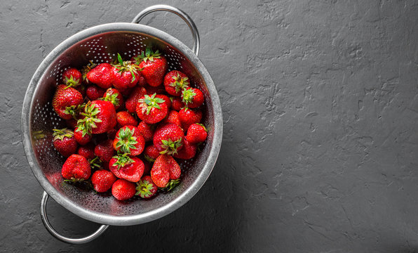 Fresh juicy red strawberries in stainless steel colander on Dark grey black slate background 
