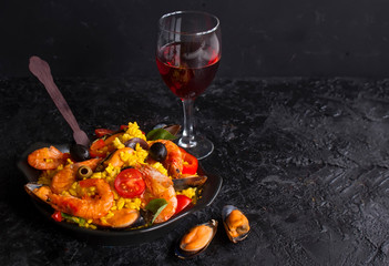 Paella on a pan with shrimp, mussels and wine on a black table. Spanish Mediterranean cuisine....