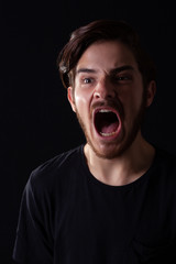 Close up of young adult male looking left screaming. Monotone, black and white for dramatic effect, dark and moody series. Concept image for terror, domestic violence, abuse, fighting.