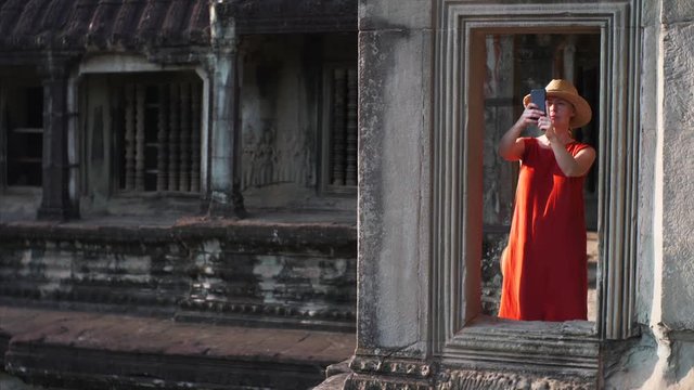 Sliding view of young woman taking photo from gallery of Angkor Wat temple built in 12th century in Cambodia and dedicated to Vishnu. Cambodia
