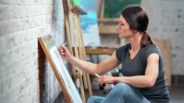 Adorable European female illustrator drawing sketch on canvas using gray pencil medium shot