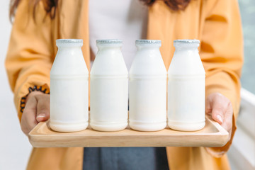 Woman holding bottles of pasteurized yogurt milk in white label color in wooden tray.