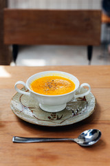 Classic Pureed Pumpkin Soup topping Pepper. Served in ceramic cup with silver spoon on wooden table.