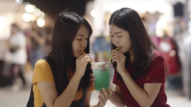 Asian young woman friends travel in Bangkok, Thailand, beautiful female feeling happy drinking cocktail at The Khao San Road. Women travel eat street food in Thailand concept. Slow motion shot.