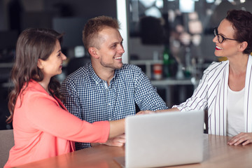 Investment adviser giving a presentation to a friendly smiling young couple seated at her desk in...