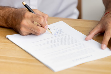 Close up caucasian male hands holding pen singing business paper
