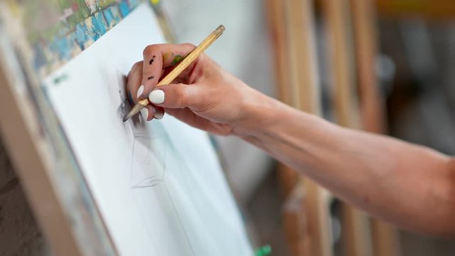 Close-up skilled female painter hand drawing sketch on white paper canvas using pencil