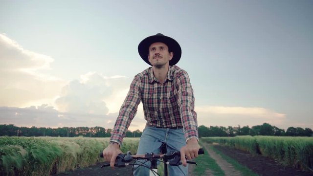 young male farmer in hat ride on the bicycle trough the wheat field 