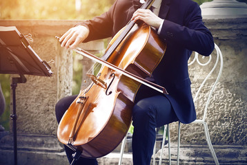 Musician in a black suit sitting on a white elegant chair on the terrace in the Park and playing classical music on string-bow the instrument - cello. ©  Valeri Vatel