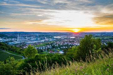 Germany, Orange summer sunset over skyline of downtown stuttgart city and arena from above in green nature landscape