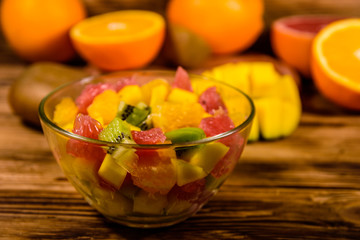 Salad with mango, oranges, grapefruit and kiwi fruits in a glass bowl on wooden table