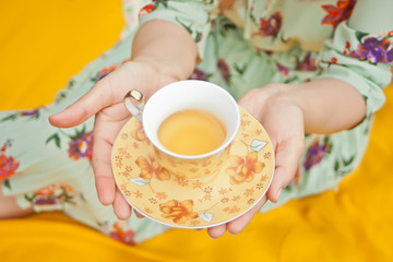 Woman on the picnic sits on the yellow cover and holds cup of tea.