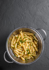 cooked Penne rigate pasta in stainless steel colander on Dark grey black slate background with copy space. top view