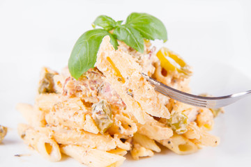 Pasta eaten with a fork - penne with white cream sauce with bacon and jalapeño peppers on a plate, decorated with fresh basil	