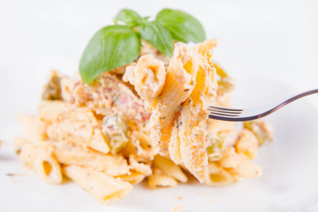 Pasta eaten with a fork - penne with white cream sauce with bacon and jalapeño peppers on a plate, decorated with fresh basil	