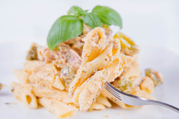Pasta eaten with a fork - penne with white cream sauce with bacon and jalapeño peppers on a plate, decorated with fresh basil	