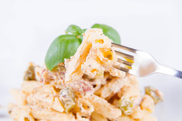 Pasta eaten with a fork - penne with white cream sauce with bacon and jalapeño peppers on a plate, decorated with fresh basil	
