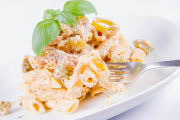 Pasta eaten with a fork - penne with white cream sauce with bacon and jalapeño peppers on a plate, decorated with fresh basil	
