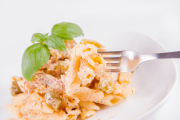 Pasta eaten with a fork - penne with white cream sauce with bacon and jalapeño peppers on a plate, decorated with fresh basil	