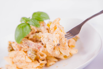 Pasta eaten with a fork - penne with white cream sauce with bacon and jalapeño peppers on a plate, decorated with fresh basil	