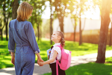 Parent and pupil of primary school go hand in hand. Woman and girl with pink backpack behind the...