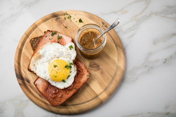 Gebräunter Bayrischer Leberkäse mit gebratenen Spiegelei auf Sonnenblumenkernbrot mit süßen Senf auf Holzbrett