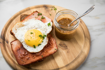 Gebräunter Bayrischer Leberkäse mit gebratenen Spiegelei auf Sonnenblumenkernbrot mit süßen Senf auf Holzbrett