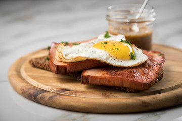 Gebräunter Bayrischer Leberkäse mit gebratenen Spiegelei auf Sonnenblumenkernbrot mit süßen Senf auf Holzbrett