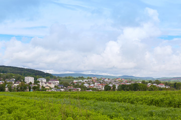 Image of best place of world, village in mountains, photo of nature scenary, blue sky with clouds, green grass and many houses on bottom of hills, sunny summer day, wonderful landscape.