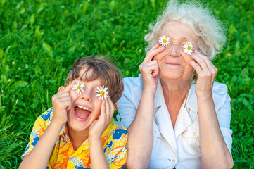 Happy grandmother and laughing   grandchild fooling around the law of putting chamomiles instead of...