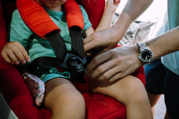 Fototapeta na wymiar Adult fastening the seat belt of the child in the car to drive safely