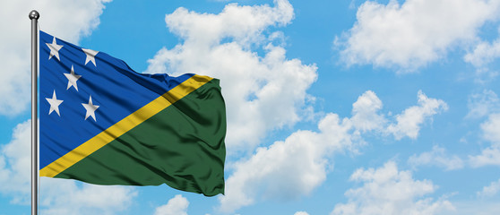 Solomon Islands flag waving in the wind against white cloudy blue sky. Diplomacy concept, international relations.