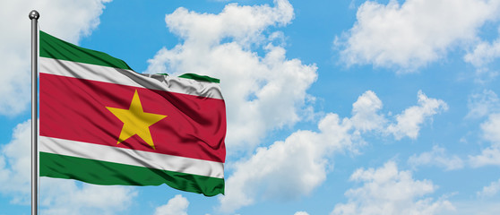 Suriname flag waving in the wind against white cloudy blue sky. Diplomacy concept, international relations.