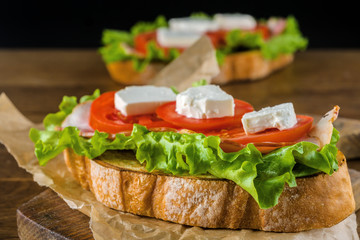 Delicious sandwich and lager beer on wooden table with dark background.