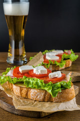 Delicious sandwich and lager beer on wooden table with dark background.