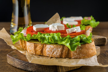 Delicious sandwich and lager beer on wooden table with dark background.