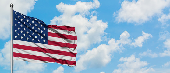 United States flag waving in the wind against white cloudy blue sky. Diplomacy concept, international relations.