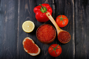 red caviar on wooden cup, wooden spoon  and vegetables on wooden background. top view